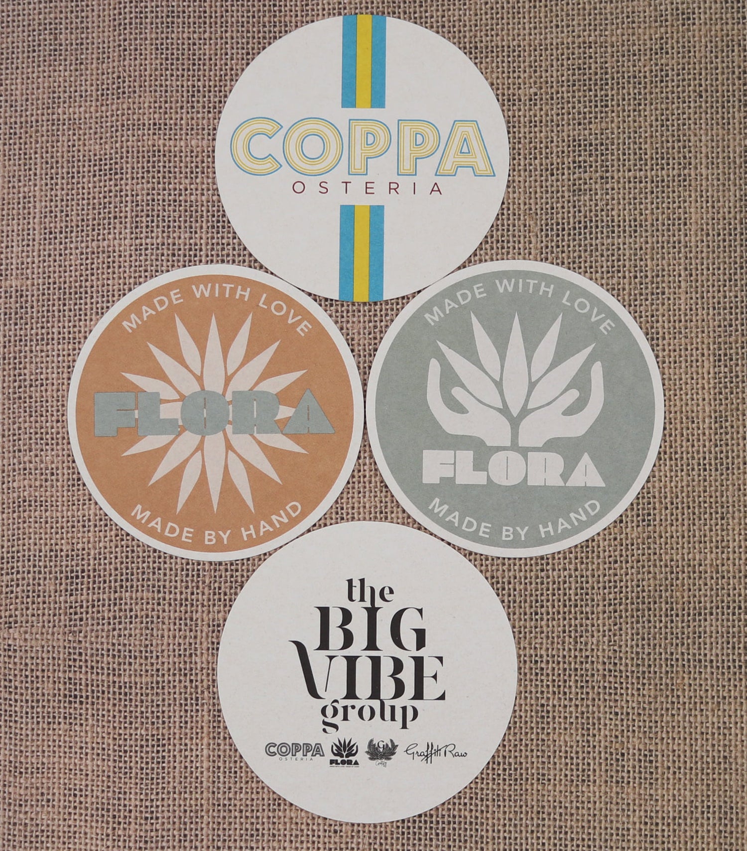 Various printed coasters, laid out in a pattern. Among the brands listed on the coasters are "Coppa Osteria," "Flora," and "The Big VIbe Group."